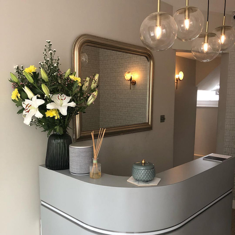 salon reception desk in grey with gold mirror and flower vase on top